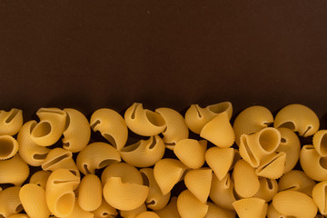 italian pasta pepe rigate, snails, scattering on a brown background, copy space from above