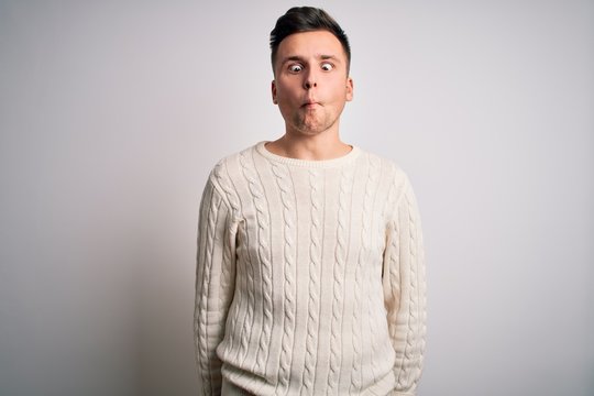 Young handsome caucasian man wearing casual winter sweater over white isolated background making fish face with lips, crazy and comical gesture. Funny expression.