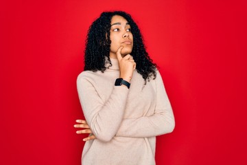Young african american curly woman wearing casual turtleneck sweater over red background with hand on chin thinking about question, pensive expression. Smiling with thoughtful face. Doubt concept.
