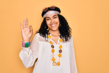 Young african american curly hippie woman wearing sunglasses and vintage accessories smiling positive doing ok sign with hand and fingers. Successful expression.