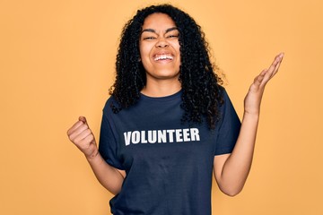 Young african american curly woman doing volunteering wearing volunteer t-shirt screaming proud and...