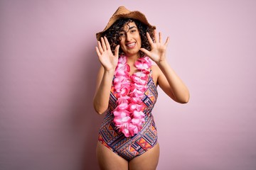 Young beautiful arab woman on vacation wearing swimsuit and hawaiian lei flowers showing and pointing up with fingers number ten while smiling confident and happy.