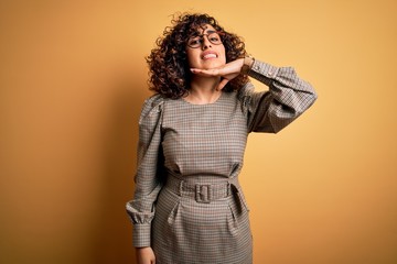 Beautiful arab business woman wearing dress and glasses standing over yellow background cutting throat with hand as knife, threaten aggression with furious violence