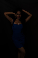 Fototapeta na wymiar Fashion portrait of an young brunette Indian Bengali woman in vibrant blue western dress in dark studio copy space background. Indian lifestyle and fashion.