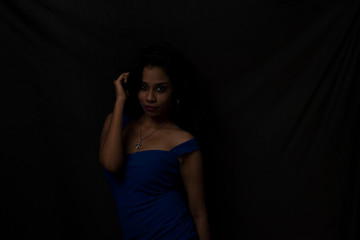 Fashion portrait of an young brunette Indian Bengali woman in vibrant blue western dress in dark studio copy space background. Indian lifestyle and fashion.