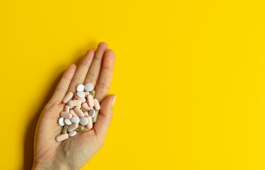 Pills in one hand on yellow background with copy space