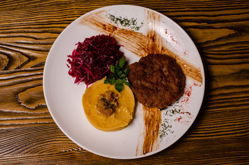 closeup two pieces of medium raw grilled meat decorated with red pepper and sauce served with potato chips and vegetable salad on black restaurant plate on wooden table.