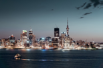 Panorama of Auckland city during blue hour with city lights reflecting in the water and a yacht...