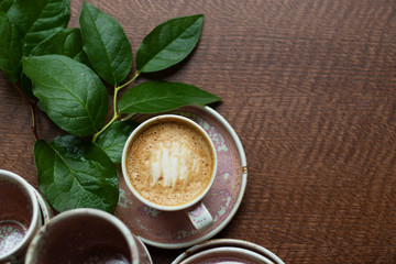 A cup of coffee with milk foam. Cappuccino stands among other dishes of the same color on the table. A branch of greenery decorates the composition. Top View and copy space