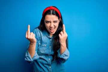 Young brunette woman wearing casual denim shirt over blue isolated background Showing middle finger doing fuck you bad expression, provocation and rude attitude. Screaming excited