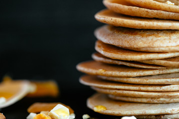 Sweet homemade stack of pancakes with honey filling, almonds and dried apricots, plate on black...