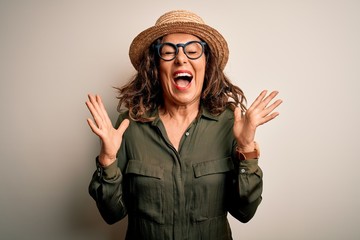 Middle age brunette woman wearing glasses and hat standing over isolated white background...