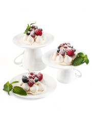 food photography of still life with Pavlova (pav) meringue mini cakes on porcelain dishes with fresh berries and mint under powdered sugar on a white background isolated