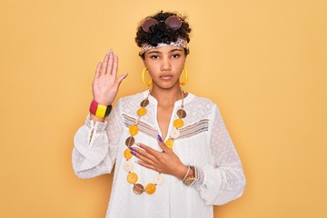 Young beautiful african american afro hippie woman wearing sunglasses and accessories Swearing with...