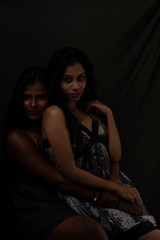 Two black and white attractive young brunette Indian Bengali women in  western wear are standing together in black studio copy space  background. Indian lifestyle and fashion.