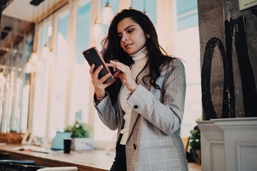Millennial female blogger in stylish clothing checking smartphone notification for update cell...