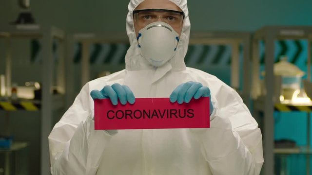 Portrait of masked laborant . Concept of coronavirus quarantine. MERS-Cov. Novel coronavirus. Doctor with a overall safety uniform Tear the red paper with the word coronavirus. COVID-2019 or nCoV2019
