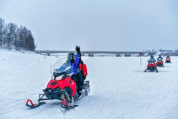 Fotobehang People on snowmobile waving hand at frozen lake winter Rovaniemi © Roman Babakin