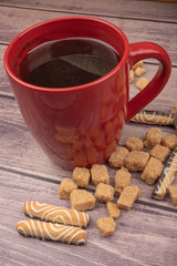 Red ceramic tea mug, cookies and pieces of cane sugar on a wooden background. Close up.