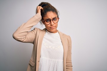 Beautiful african american businesswoman wearing jacket and glasses over white background confuse and wonder about question. Uncertain with doubt, thinking with hand on head. Pensive concept.