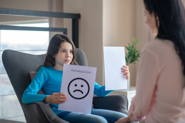 Long-haired teen in a blue shirt holding a table with a sad face