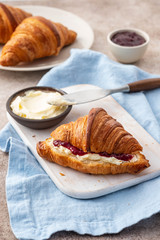 fresh breakfast - raspberry jam and croissant on a white board.