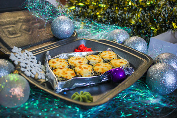 Baked rolls in a black container with ginger and wasabi with silver new year balls and artificial snowflake. Lunch in New Year's decoration