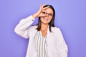 Young beautiful brunette psychologist woman wearing coat and glasses over purple background doing ok gesture with hand smiling, eye looking through fingers with happy face.