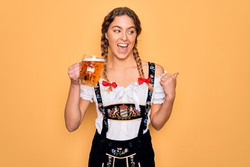 Beautiful blonde german woman with blue eyes wearing octoberfest dress drinking jar of beer pointing and showing with thumb up to the side with happy face smiling