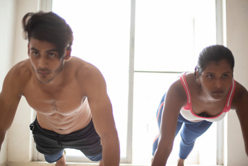 Fototapeta na wymiar An young Indian Bengali brunette man and dark skinned woman with muscular body doing exercise in a room in white background. Fitness and Indian lifestyle.