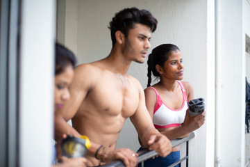 An young Indian Bengali group of friends/siblings are enjoying themselves standing on the balcony after work out in white background. Indian lifestyle.