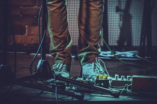 Closeup of the feet of a person near guitar pedals and a mic stand under the lights