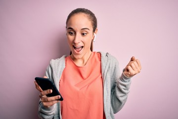 Fototapeta premium Beautiful sporty woman doing sport listening to music using earphones over pink background screaming proud and celebrating victory and success very excited, cheering emotion