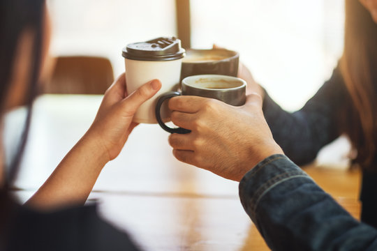 Closeup image of people enjoyed drinking and clinking coffee cups on the table in cafe