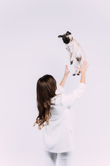 A laughing and smiling auburn haired woman in a white dress, is staring most lovingly at her cute pug, who calmly sits on the hands, gaining her undivided attention. Isolated white background.