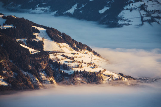 Nebelmeer mit goldenem Sonnenaufgangslicht und kleinen H&uuml;tten auf H&uuml;gel oberhalb der Wolken. 