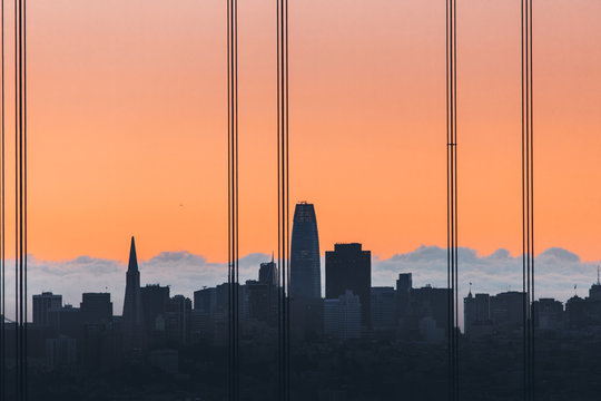 Goldener Sonnenaufgang mit Streben der Golden Gate Bridge im Vordergrund sowie Skyline von San Francisco im Hintergrund 