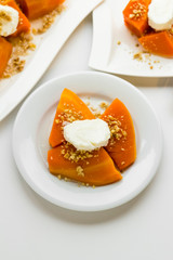Traditional Turkish Pumpkin Dessert on the white surface.Cream and chopped walnuts topping.Vertical image