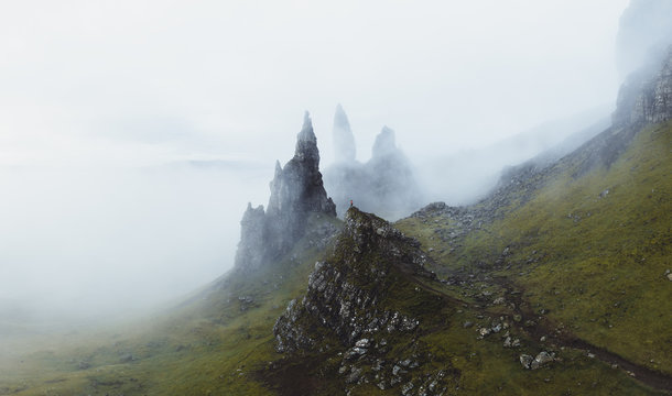 Luftaufnahme von Bergsteiger vor  Old Man of Storr Schottland in gr&uuml;ner H&uuml;gellandschaft umh&uuml;lt mit Nebel und See im Hintergrund. 