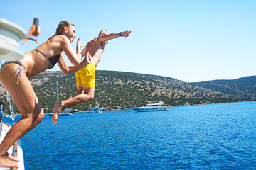 Young couple diving into the turquoise water of the sea from yacht.