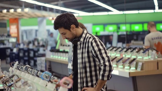 Pretty female consultant gives professional advice to a young man. He considers to buy a new smartphone and needs expert opinion. Store is modern, bright and has all the new devices. Blurred