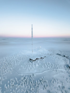 Haus mit großem Sendemast in verschneiter Landschaft umrundet von verschneiten Bäumen auf Hügel und Nebel im Hintergrund am Polarkreis. 