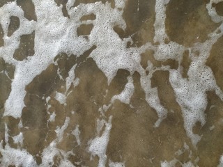 Turbulent sea water mixed with foam washing over sand