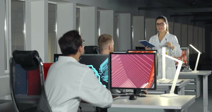 Woman engineer in lab coat instructing apprentices in office