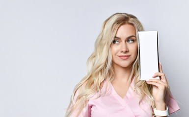 Fototapeta premium Blond woman with lovely makeup posing isolated on white. Smiling, holding a package of cosmetic product near the face with copy space for your text, logo.