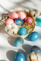 Easter decorations. Painted eggs in sunlight on a white background. Dyed eggs in the nest in the sunshine.