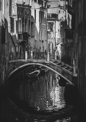 Streets of Venice in black and white monochrome with traditional houses and a bridge reflecting on the waterway of the city 