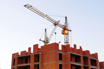 Two cranes near building. Building under construction. Construction site. Red brick building under construction.