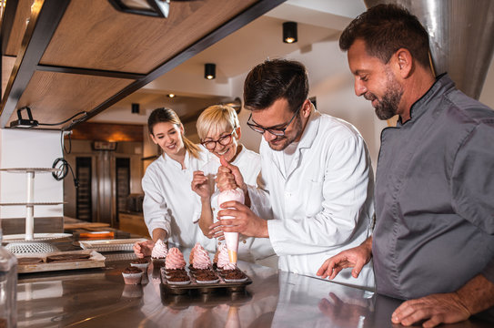 Group of workers in uniform decorating desserts in modern manufacturing.