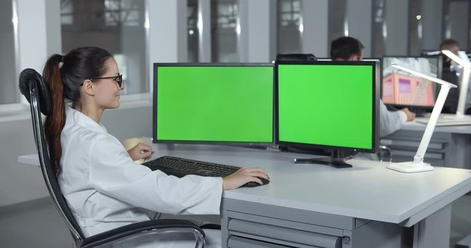 Woman in lab coat sitting at desktop with computer in laboratory